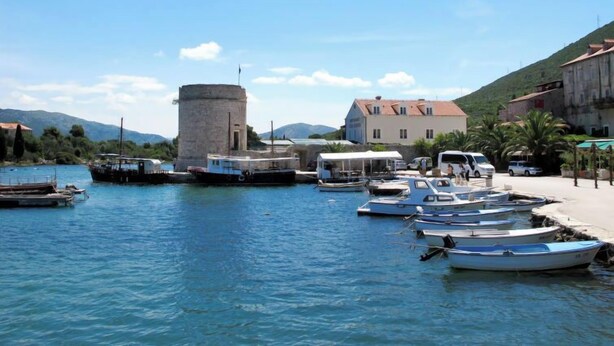 Un puerto con barcos amarrados, una torre de piedra y edificios a lo largo del muelle.