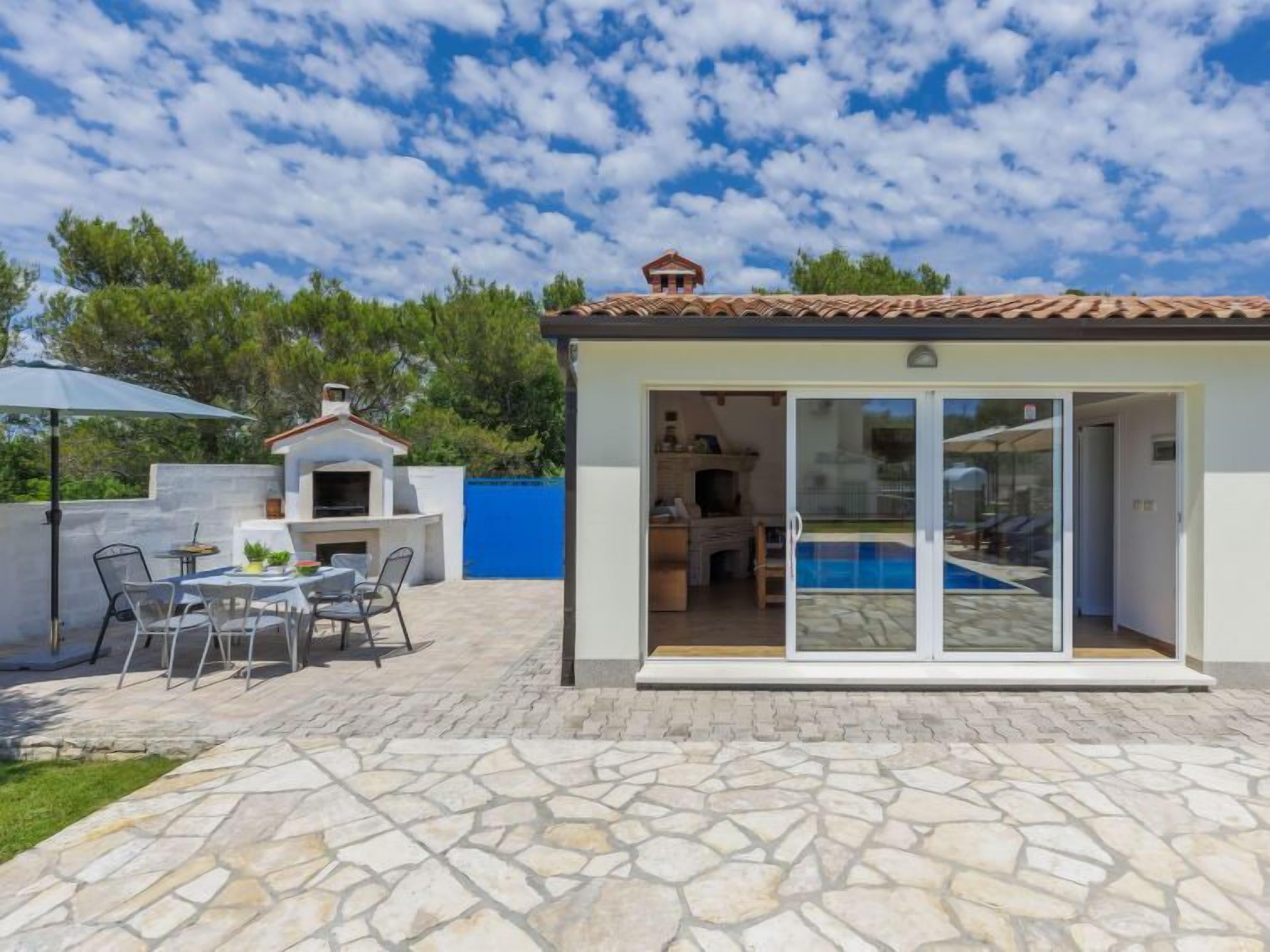 Ett modernt hus med en uteplats, utomhusmöbler, en swimmingpool och en entré med glasdörr.
