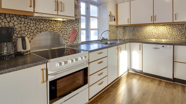 Uma cozinha moderna com armários brancos, painel de pedra e piso de madeira.