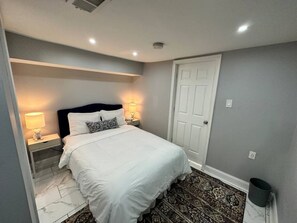 Um quarto com uma cama, mesas de cabeceira, uma porta e um tapete estampado.