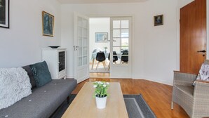 A modern living room with a sofa, a coffee table with a plant, and a dining area visible through an open door. - "Borka" - 150m from the sea by Interhome (Skagen)