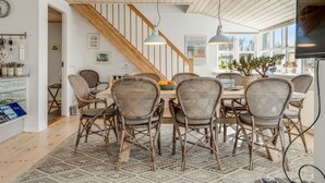 A dining area with wicker chairs, a wooden staircase, and a large window.