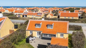 A coastal residential area with orange-roofed houses, a paved driveway, and a grassy lawn.