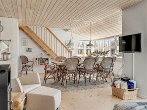 A modern living room with a dining area, wooden ceiling, and a TV mounted on the wall.