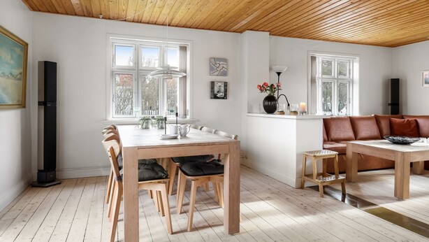 Un vaste espace de vie doté d’un plafond en bois, d’une table à manger avec des chaises, d’un canapé et d’une cheminée.