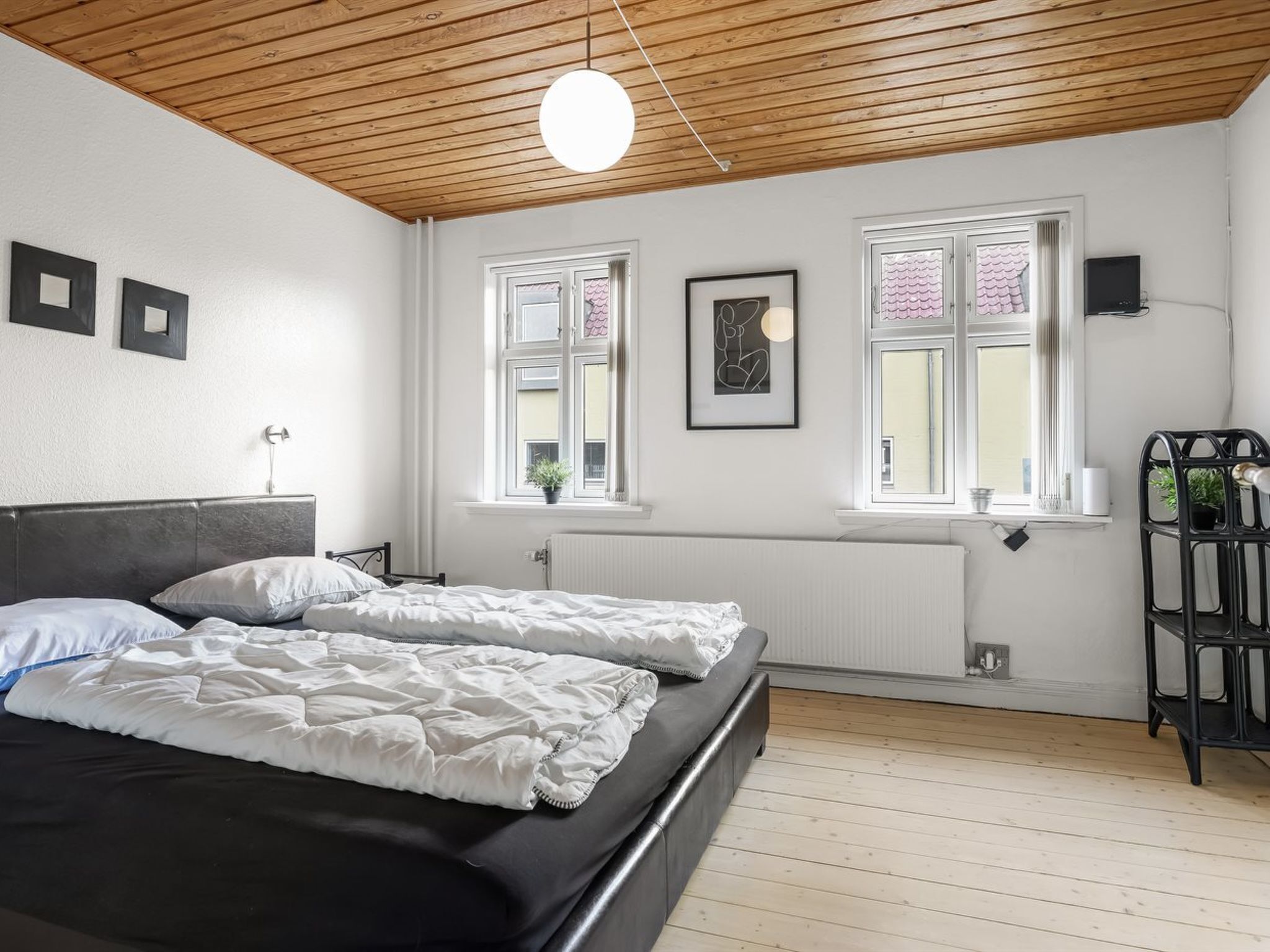 A bedroom with two beds, a wooden ceiling, a radiator, and a window with curtains.
