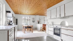 Une cuisine moderne avec des meubles blancs, un plafond en bois et un coin repas comprenant une table et des chaises.