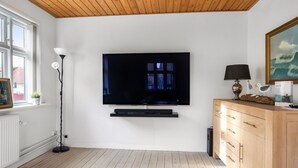 Un salon moderne avec un téléviseur à écran plat fixé au mur, un plancher en bois, un plafond en bois, un mur blanc, un meuble en bois, une lampe sur pied et un tableau encadré.