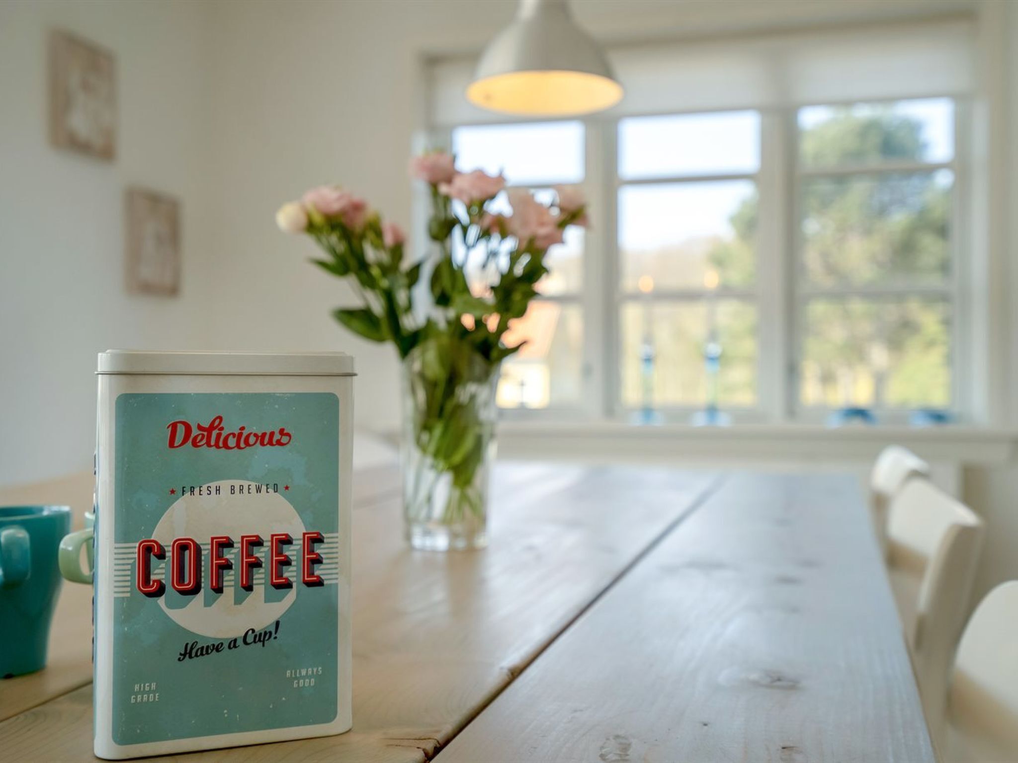 Un récipient à café sur une table en bois, avec un vase de fleurs en arrière-plan.