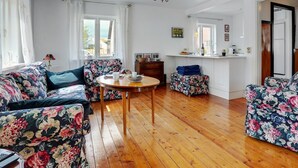 Ein Wohnzimmer mit Sofas mit Blumenmuster, einem Holztisch und einer Küchenzeile mit Spüle und Arbeitsfläche.