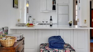 Eine kompakte Küche mit weißen Schränken, einem eingebauten Backofen und einem Kühlschrank. Es gibt einen kleinen Essbereich mit einer blumigen Tischdecke und einem blauen Handtuch.