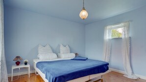 Ein Schlafzimmer mit Bett, Nachttisch, Lampe und einem Fenster mit Vorhängen.