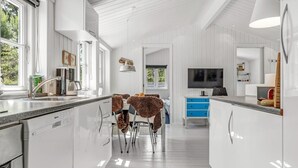 A modern kitchen with white cabinetry, a dining area with a table and chairs, and a TV mounted on the wall. - "Thorkil" - 800m from the sea by Interhome (Skagen)
