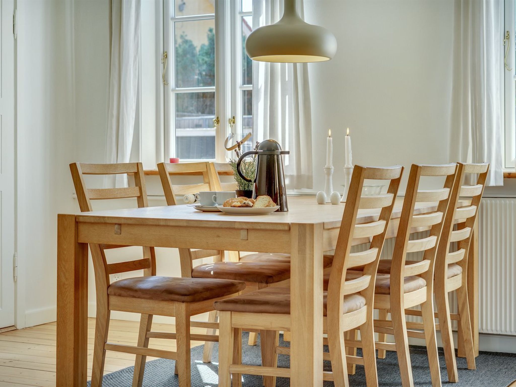 Et spiseområde med et træbord og stole, en kaffekande og stearinlys på vindueskarmen.