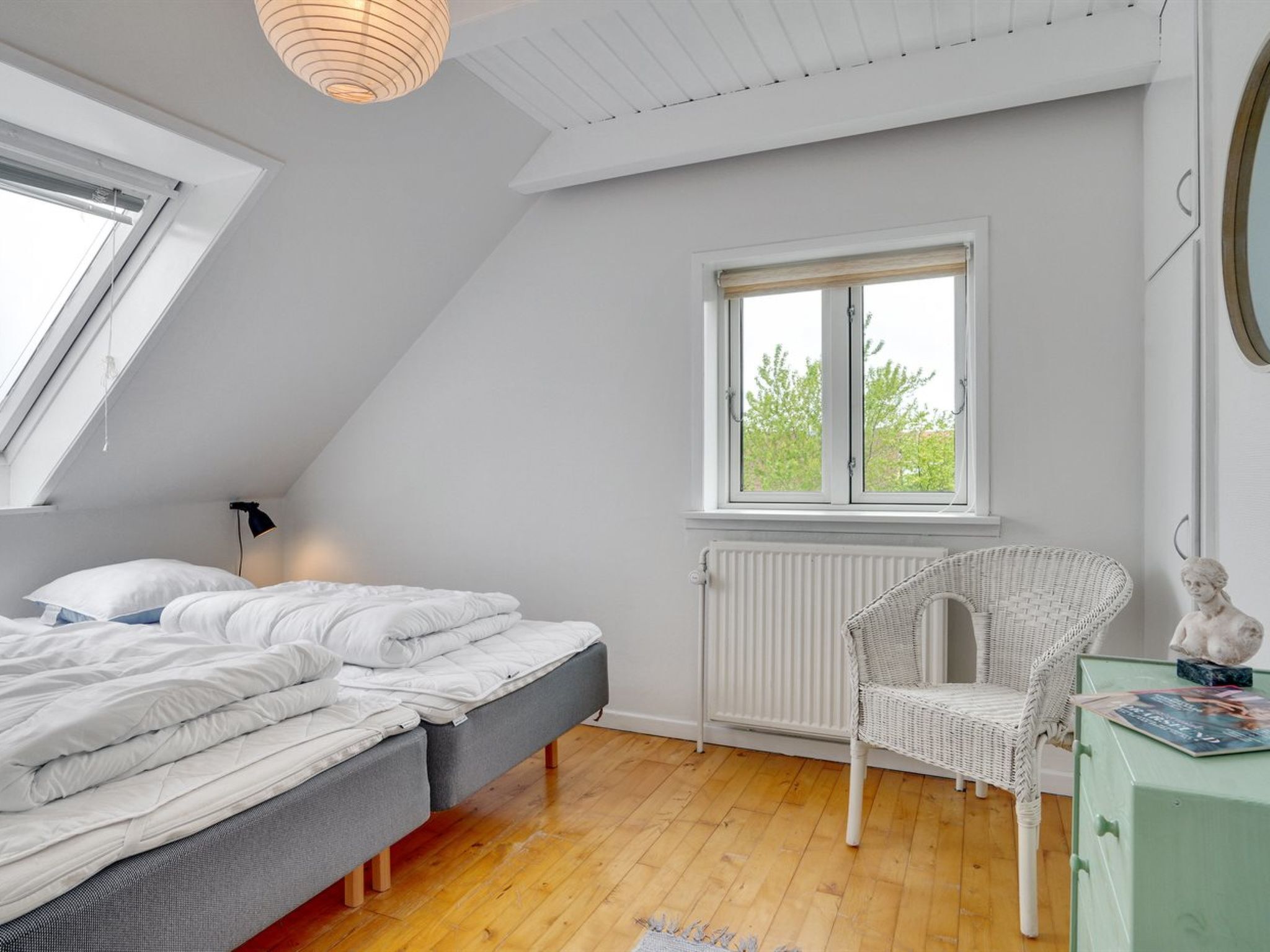 Une chambre avec un plafond en pente, un lit, une chaise et une fenêtre donnant sur un paysage verdoyant.