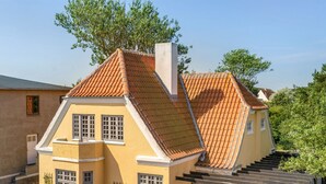 A two-story house with a red-tiled roof, a white picket fence, and a parked car in front.