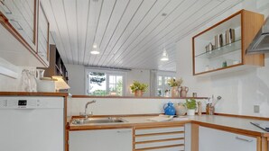 A modern kitchen with white cabinets, wooden countertops, a Bosch dishwasher, a sink, and a window with plants on the windowsill.