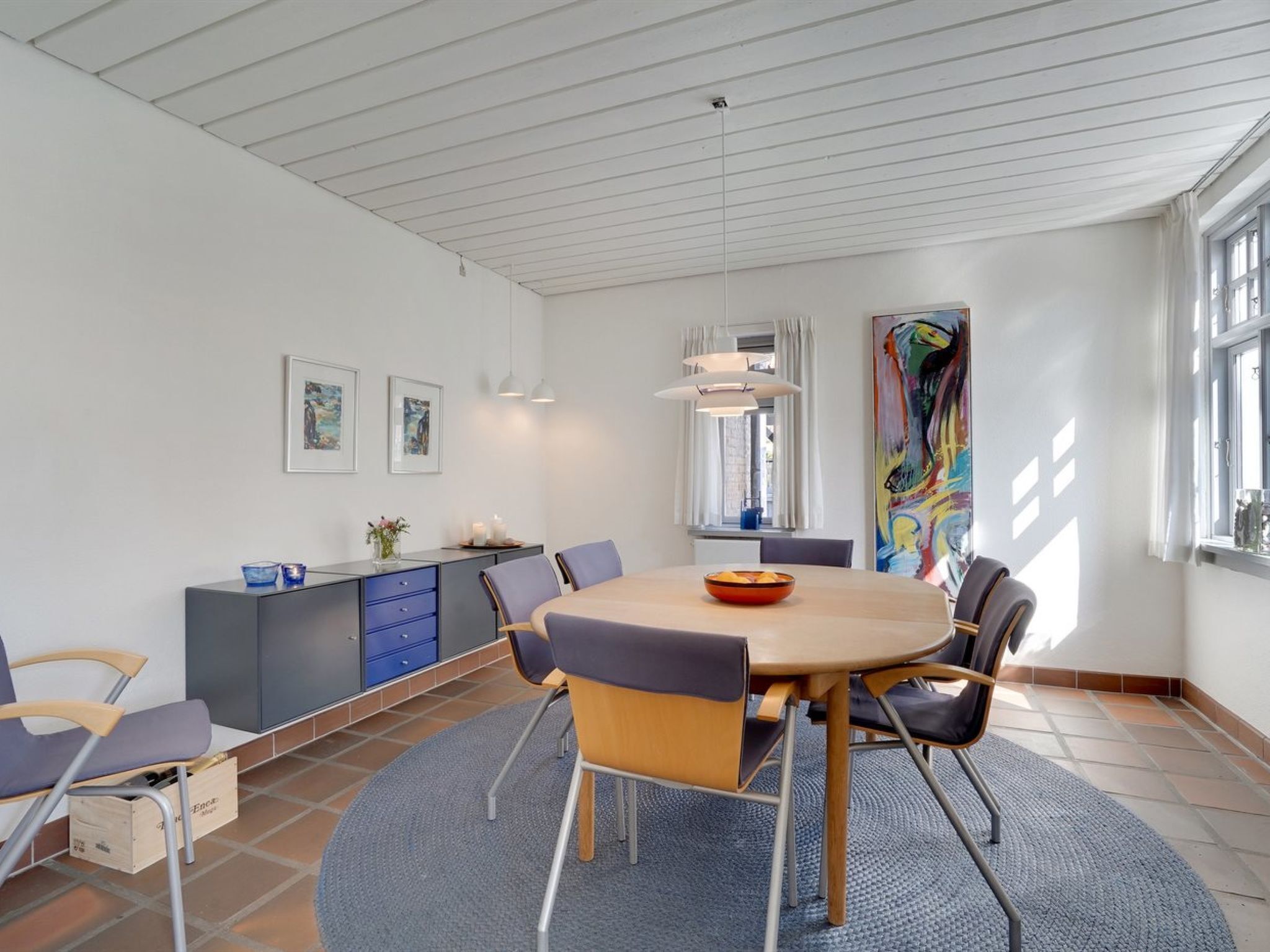A modern dining area with a round table, chairs, a blue rug, and a kitchen counter with cabinets.