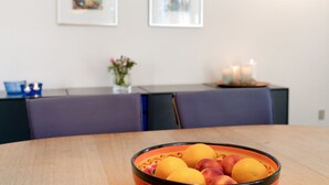 A dining table with a bowl of fruit and a candle on a side table.
