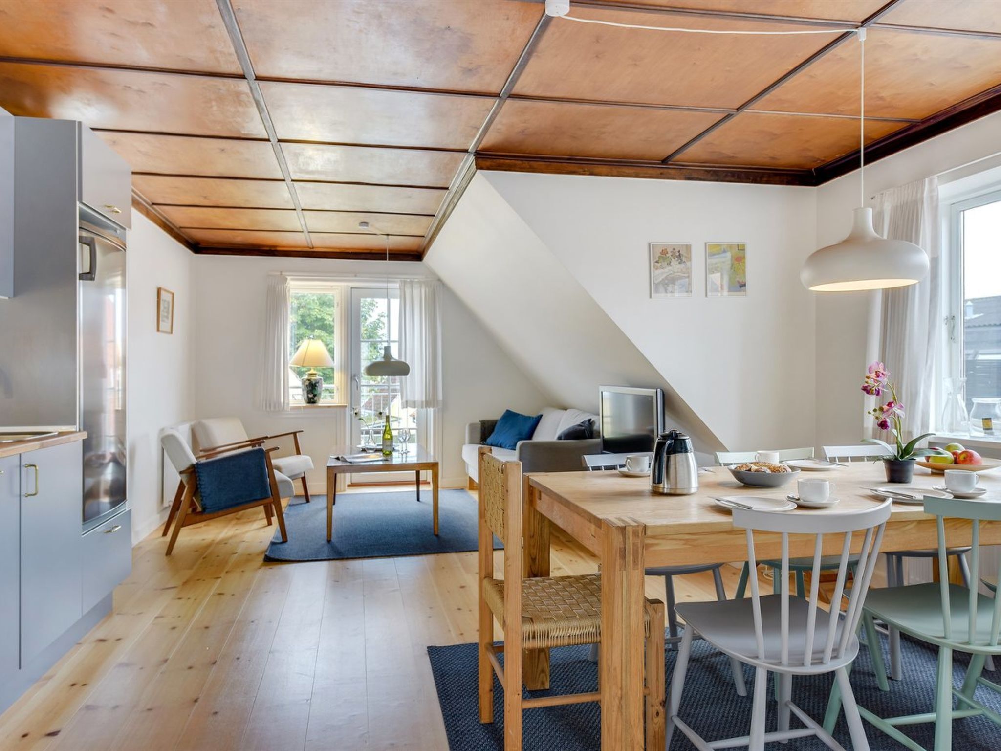 Et moderne køkken med trægulv, et spiseområde med bord og stole, samt en opholdsstue med sofa og fjernsyn.