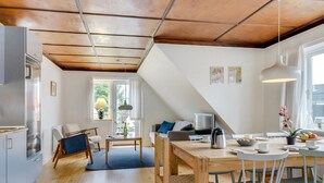 A modern kitchen with wooden flooring, a dining area with a table and chairs, and a living space with a sofa and a TV.