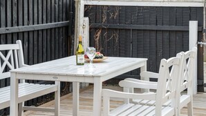 A white outdoor dining table with chairs, a bottle of wine, and a glass on the table.