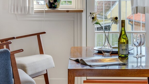 A wooden table with a wine bottle and glasses, a vase with flowers, and a chair with a towel.