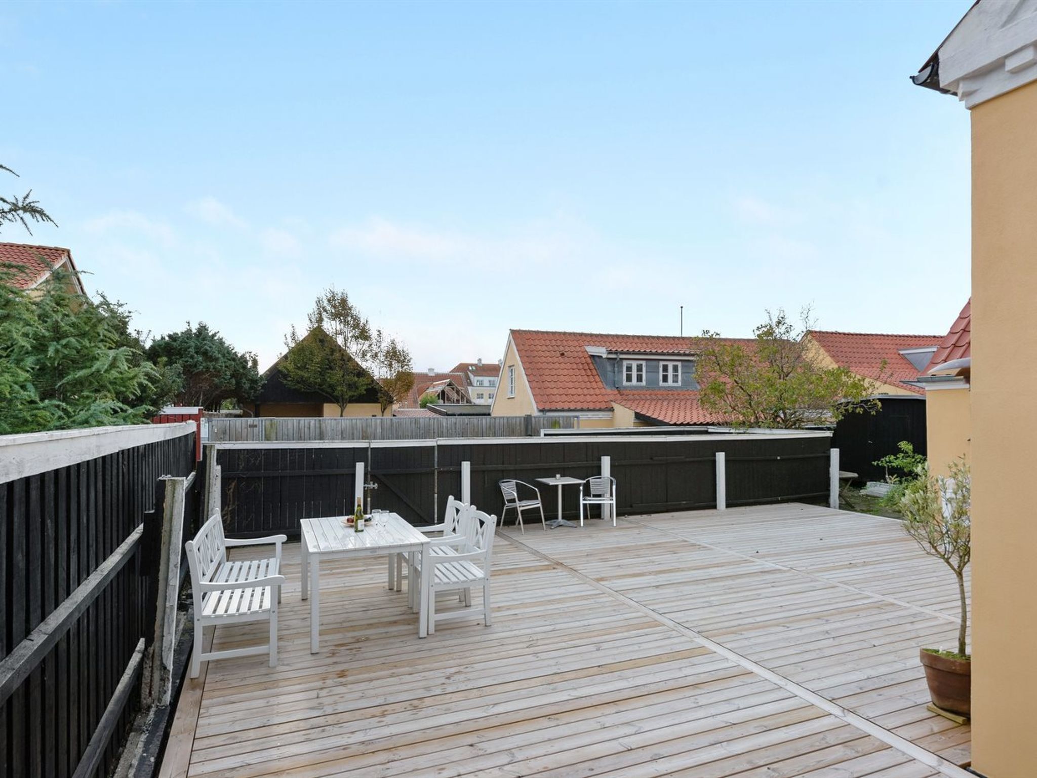 Een houten terras met een tafel en stoelen, omringd door een zwarte omheining.