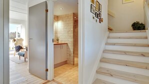 Un interior modern amb una escala de fusta, una cuina amb salabost i una zona de menjador amb una cadira i una taula.