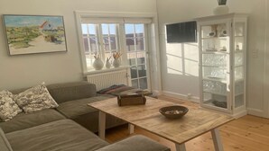 Ein Wohnzimmer mit einer Couch, einem Couchtisch, einem Schrank mit Glastüren, einem Bild an der Wand und Blick durch ein Fenster.