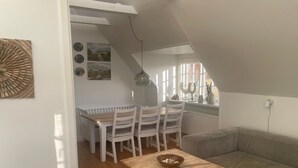 Ein Essbereich mit Holztisch und -stühlen, einem grauen Sofa und Blick ins Freie.