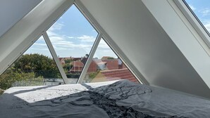 Ein Zimmer mit schrägem Dach, Dachfenstern und einem Bett mit gemusterten Betttextilien.