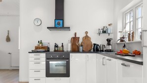 Une cuisine moderne avec des meubles blancs, un four noir, une planche à découper en bois et une machine à café.