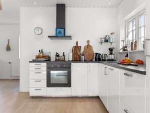 Une cuisine moderne avec des meubles blancs, un four noir, une planche à découper en bois et une machine à café.