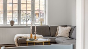 Un salon moderne avec un canapé gris, une table basse ronde et une fenêtre donnant sur des immeubles.
