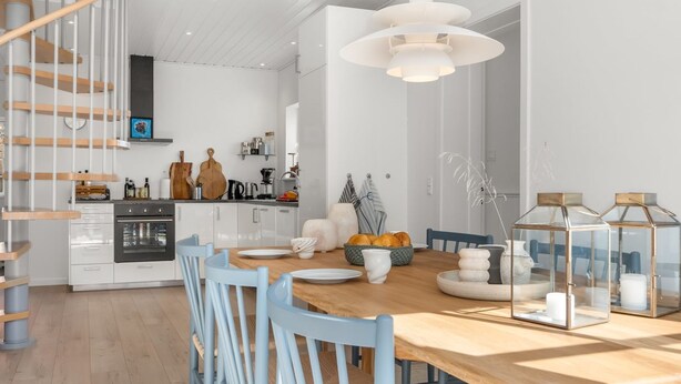 Une cuisine moderne avec des meubles blancs, une table à manger en bois, des chaises bleues et un escalier en colimaçon.