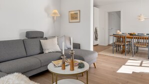 Un salon moderne avec un canapé gris, une table basse ronde et un coin repas comprenant une table et des chaises en bois.