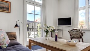 A modern living room with a sofa, a wooden coffee table, a TV, and a chair with a decorative cushion.