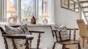 A room with two wooden chairs, a small table, and a window with two lamps.