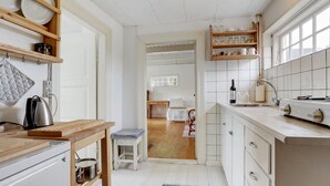A modern kitchen with white cabinetry, wooden shelves, and a dining area visible through an open door.