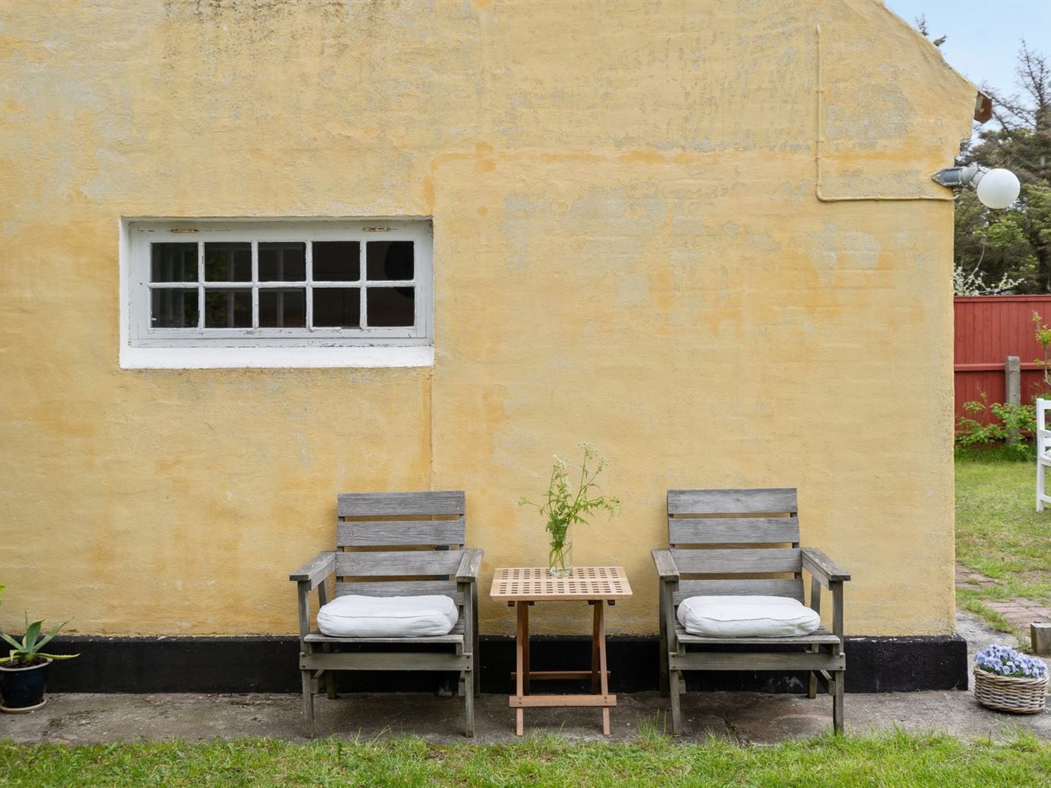 A rustic building with a yellow exterior, a small window, and two wooden benches with cushions.