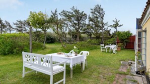 An outdoor dining area with a white table and chairs, surrounded by greenery and trees.
