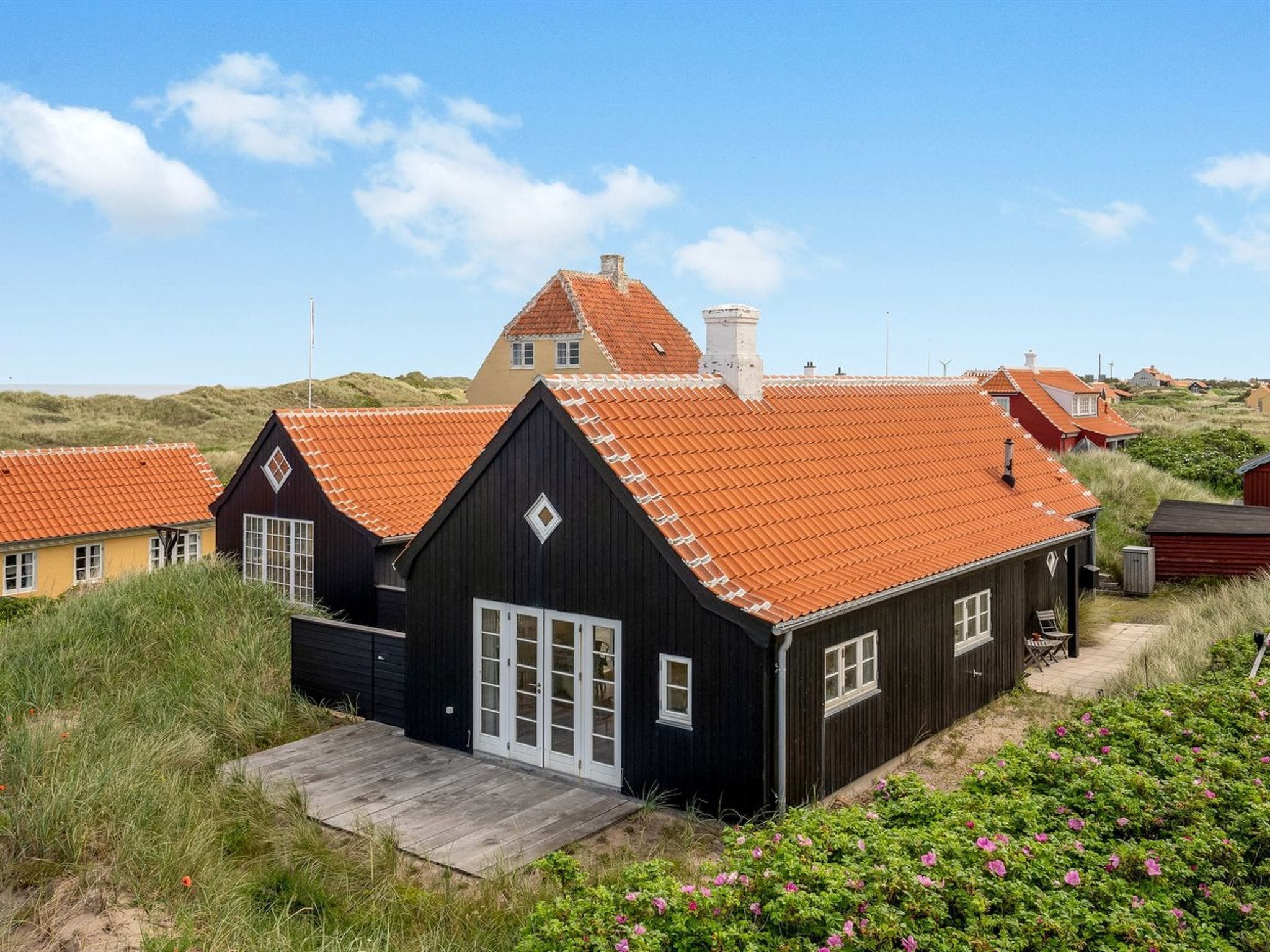 Une maison en bois peinte en noir, avec un toit recouvert de tuiles rouges, entourée de pelouse et de fleurs.