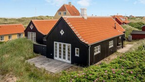 A black wooden house with a red-tiled roof, surrounded by grass and flowers.
