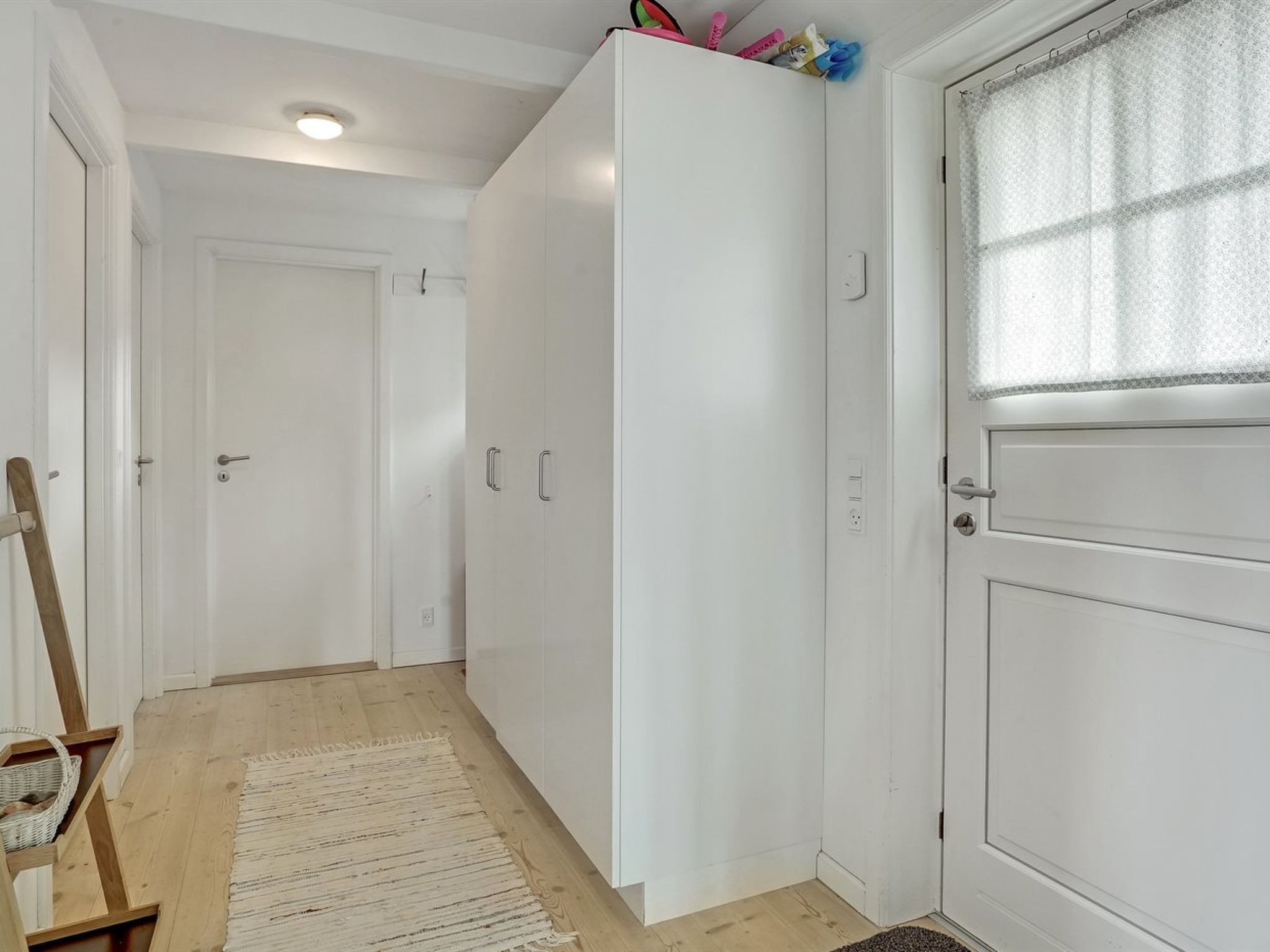 Ein Flur mit einem weißen Kleiderschrank, Holzboden und einer weißen Tür mit Fenster.