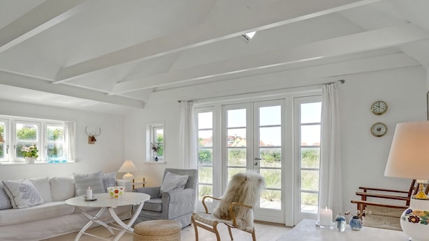A bright, spacious living room with a white sofa, a round table, and a wicker ottoman.