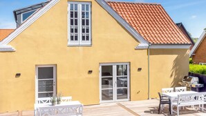 Een geel gebouw met een schuin dak, een terras met tuinmeubilair en een barbecueplek.