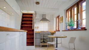 A kitchen with white cabinets, a wooden staircase, a stove, and a dining area with a table and chairs.
