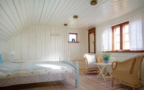Un dormitorio con cama, una silla, una mesa y una ventana.
