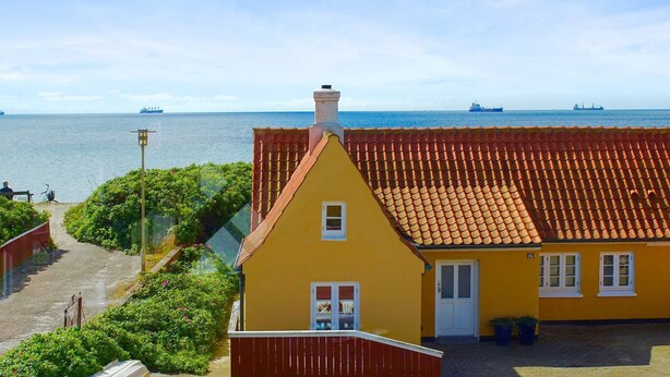 A yellow building with a red-tiled roof overlooking a body of water.